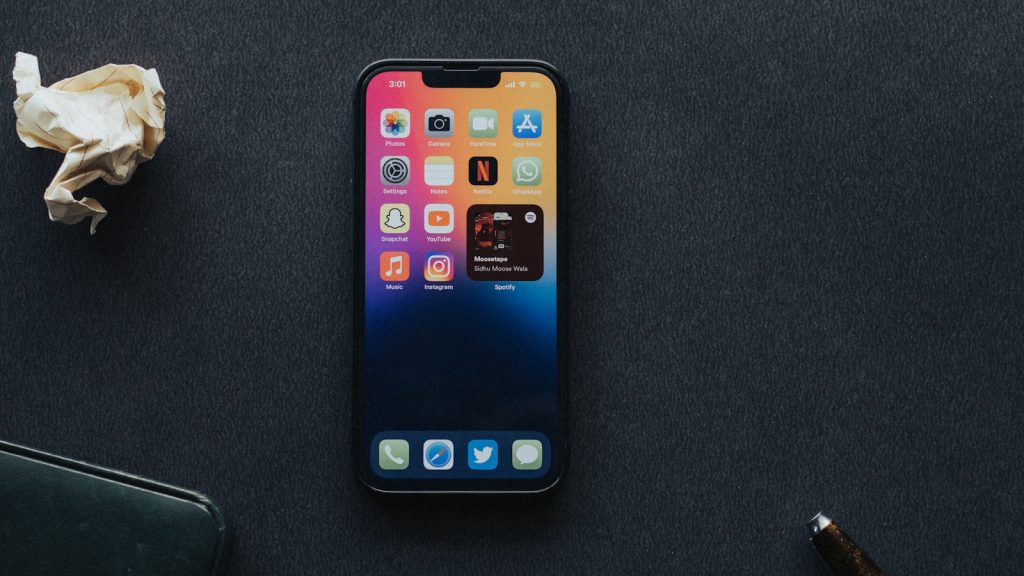 an iPhone 13 sitting on top of a table next to a pen